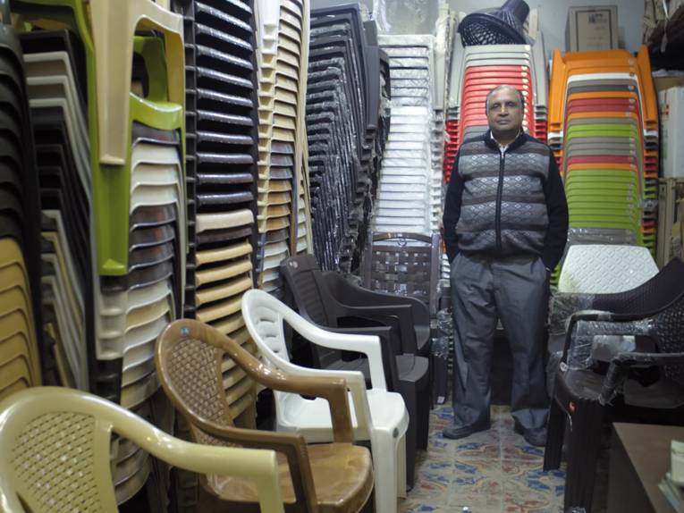 Ein Mann steht in einem Stuhllager in dem Plastikstühle unterschiedlichster Ausführungen gestapelt sind.